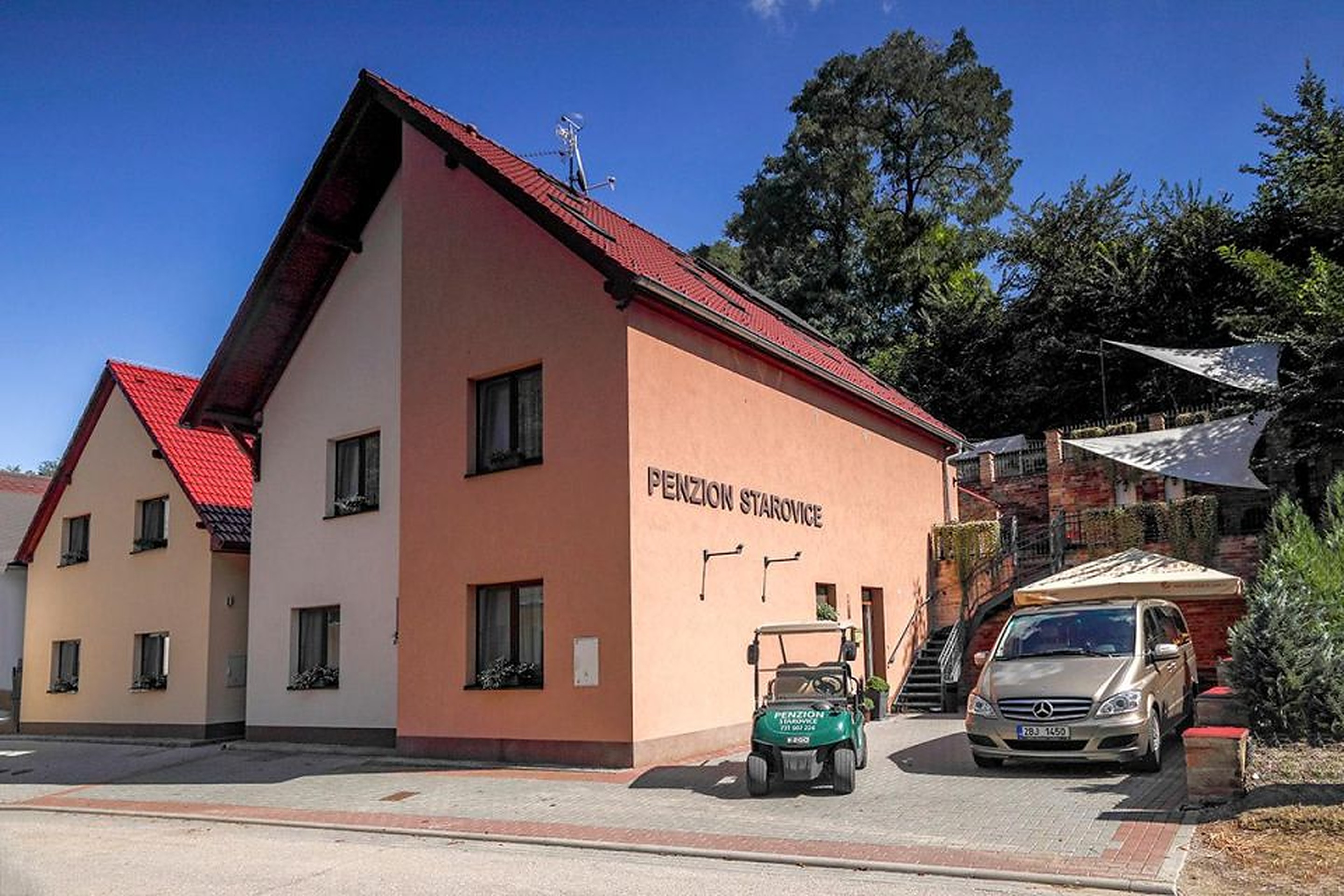 Celkový pohled na oba penziony Starovice s nádvořím, golfovým vozíkem a terasami v pozadí