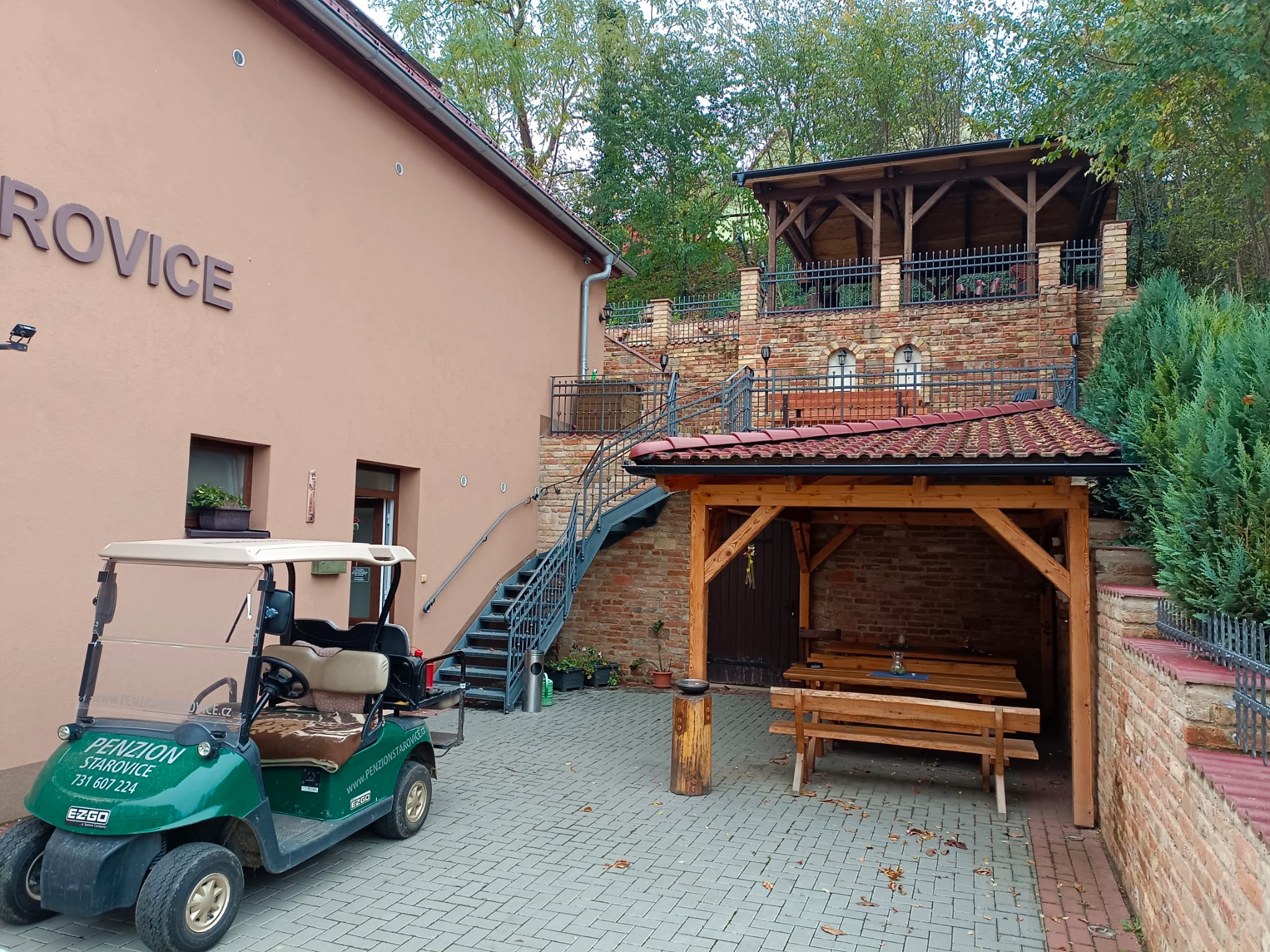 Penzion Starovice na podzim — budova s nápisem, dřevěný přístřešek a kaskádovité terasy